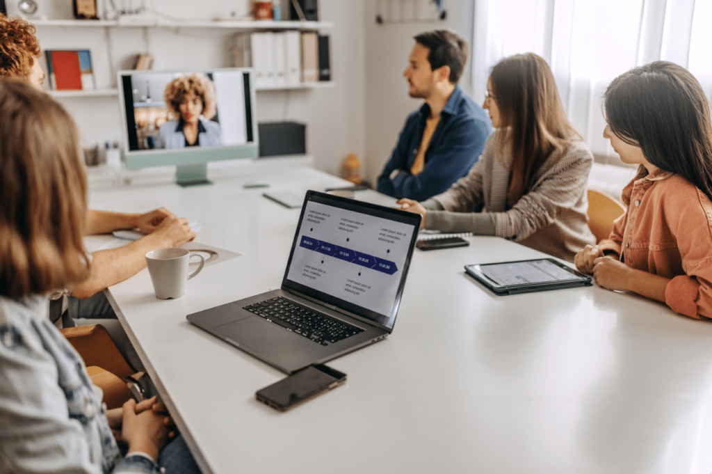 People having a video call meeting in a modern office, with a laptop and tablet on the table.