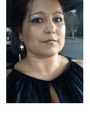 Person wearing a sleeveless black top and earrings, sitting in a car, looking towards the camera with a neutral expression.